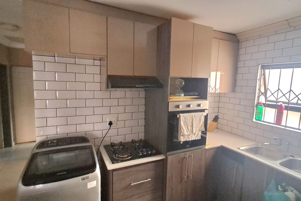 Modern kitchen featuring subway tile backsplash, built-in oven, gas hob, extractor fan, and double basin sink with security bars on the window.