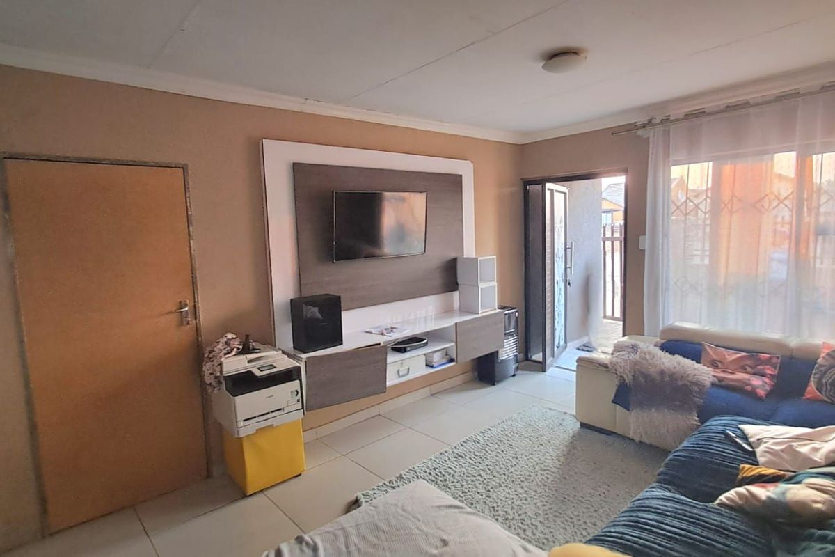 A living room featuring tiled flooring, a built-in media unit, and direct access to an outdoor area through a glass door.