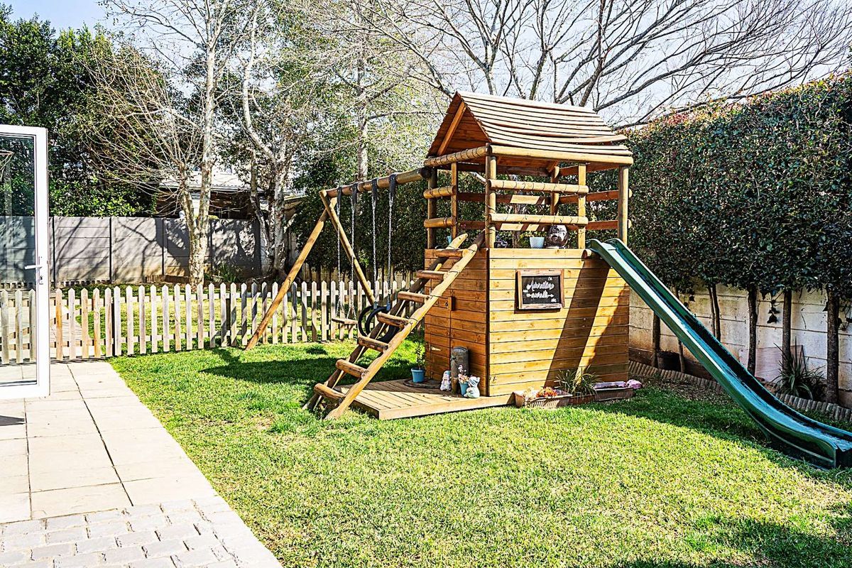 A well-maintained rear garden featuring a manicured lawn, paved patio area, and a wooden children's play structure with a slide.