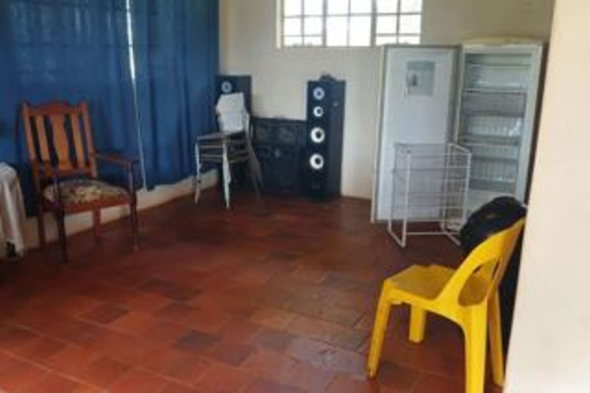 A living area featuring traditional terracotta floor tiles and large windows, providing a functional space with potential for modernization.