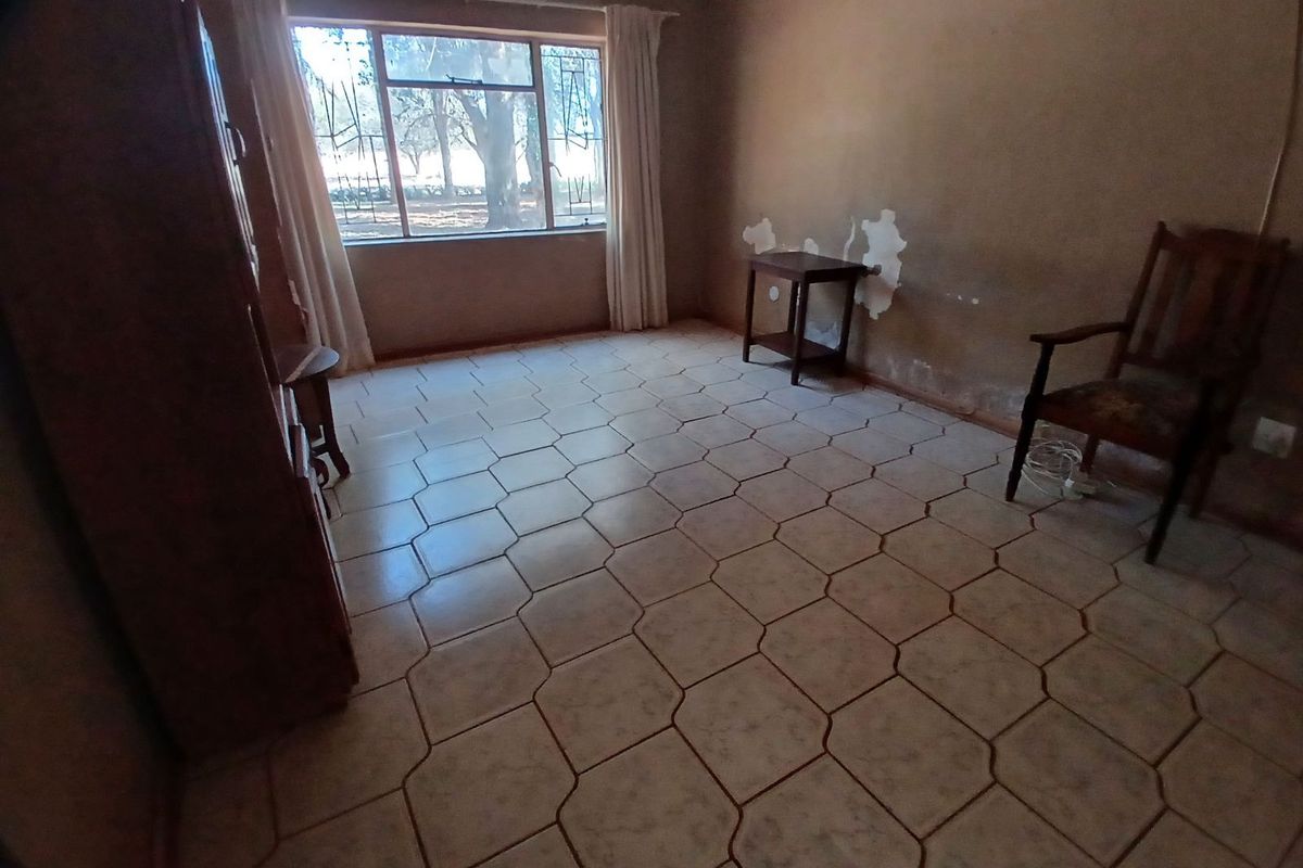 A bedroom featuring tiled flooring and a large window with security bars, currently showing signs of wear and requiring cosmetic updates.