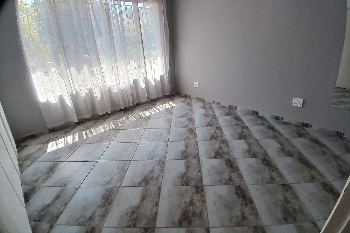 A bright, empty living room featuring modern patterned floor tiles and large windows with sheer curtains, providing a clean and neutral space.