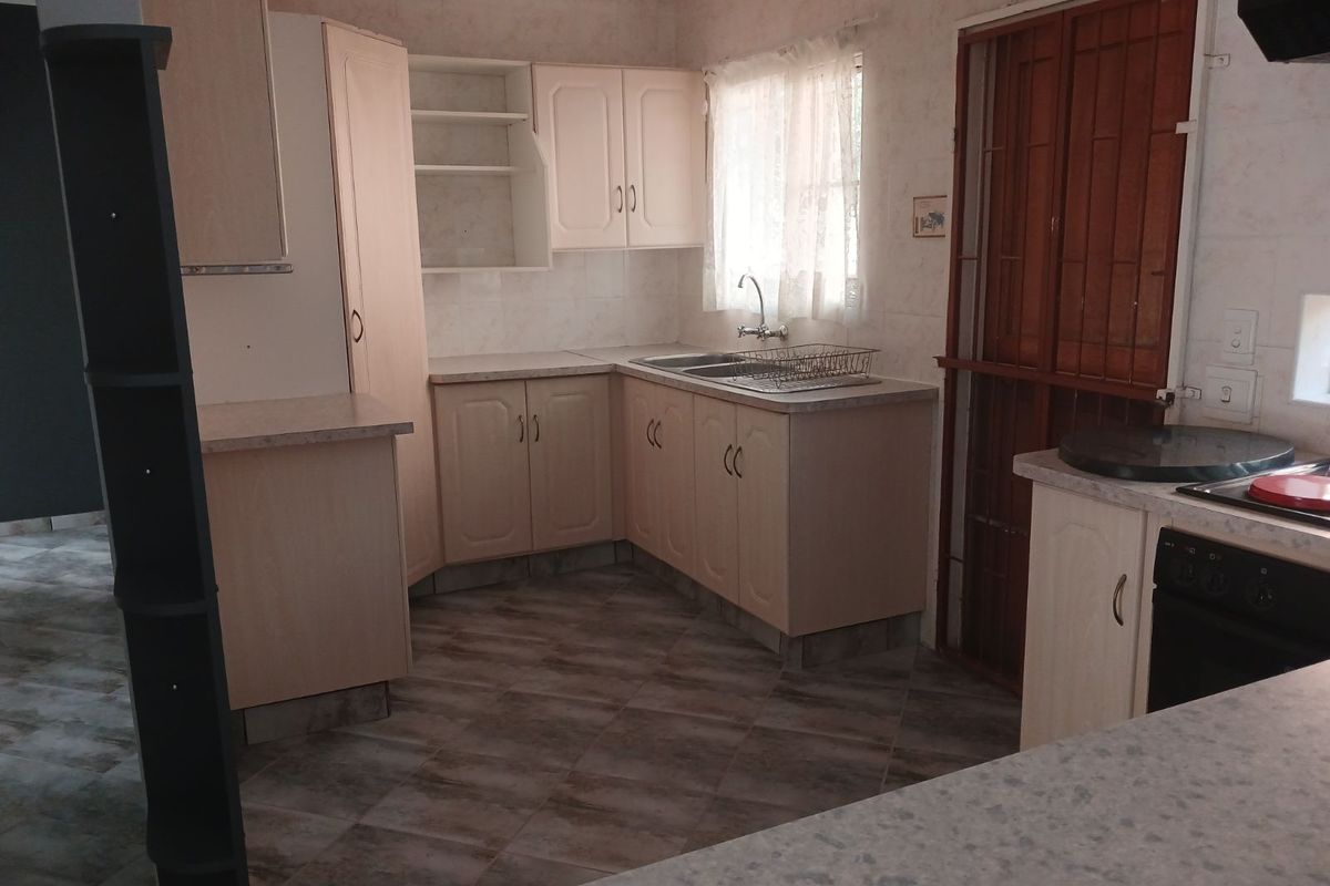 A functional kitchen featuring light-toned cabinetry, laminate countertops, a double-basin sink, and tiled flooring with a security gate at the rear entrance.