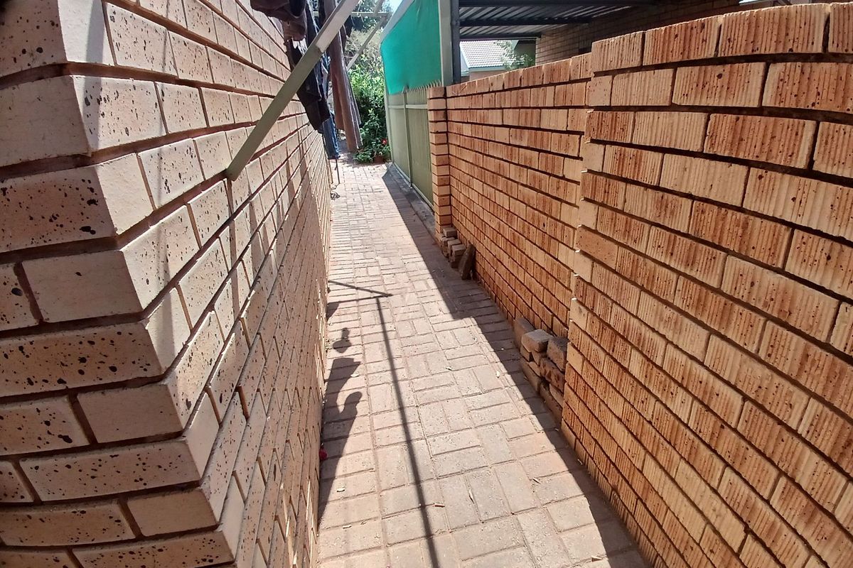 A narrow exterior side passage featuring paved flooring and face-brick boundary walls, providing access along the side of the townhouse property.