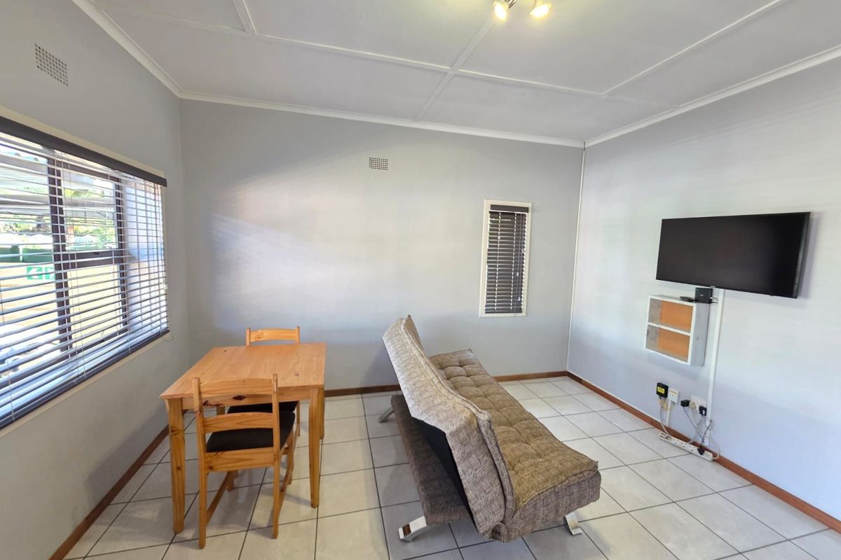 A functional living and dining area featuring tiled flooring, venetian blinds, and a wall-mounted television setup.