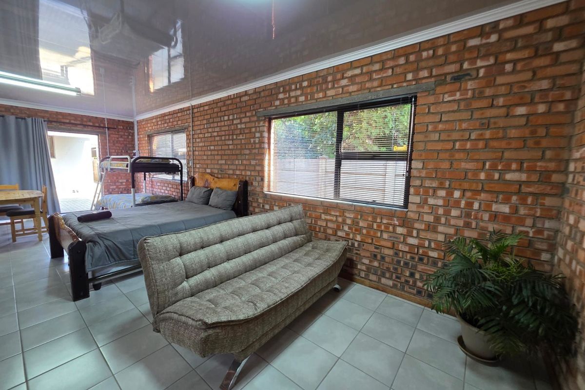 Spacious bedroom featuring exposed face-brick walls, high-gloss ceiling finish, and tiled flooring with direct access to an outdoor area.