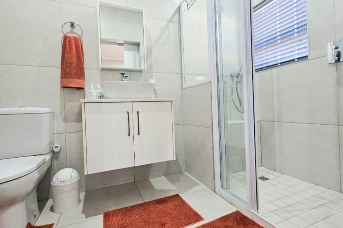 Modern bathroom featuring a wall-mounted vanity with vessel sink, a glass-enclosed walk-in shower, and neutral floor-to-ceiling tiling.