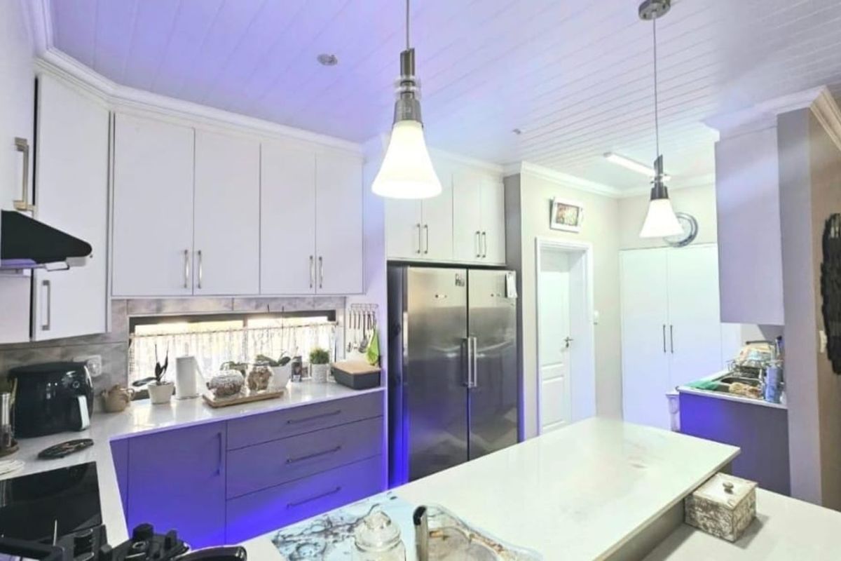 Modern kitchen featuring white cabinetry, stone countertops, a central island, and integrated stainless steel appliances under a panelled ceiling.