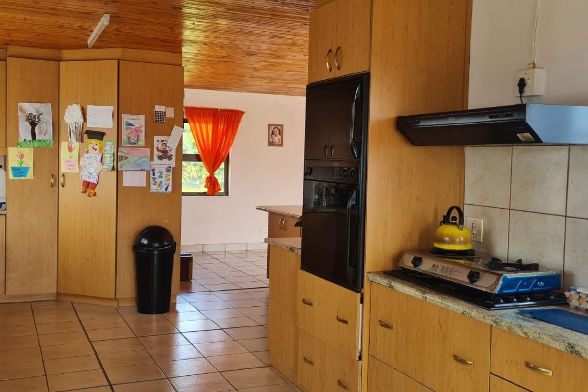 A functional kitchen featuring wooden cabinetry, built-in oven, extractor fan, and tiled flooring, with an open-plan layout leading to the living area.