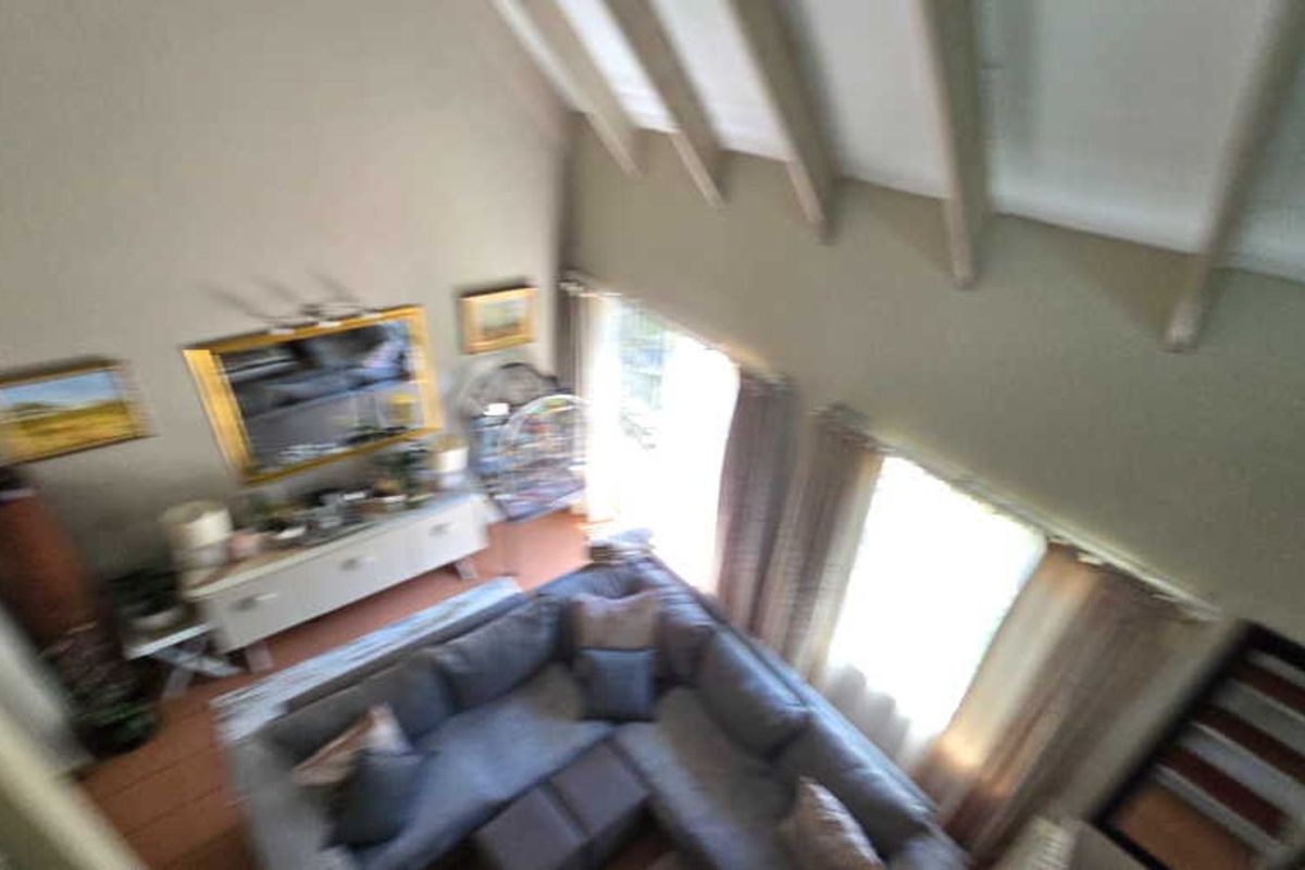 High-angle view of a living room featuring a double-volume ceiling with exposed rafters and large windows allowing natural light.