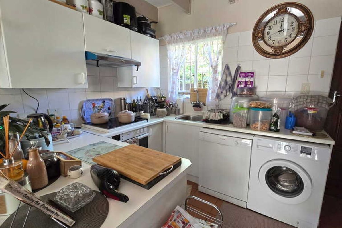 A functional kitchen featuring white cabinetry, integrated stove and extractor fan, stainless steel sink, and dedicated space for laundry appliances.