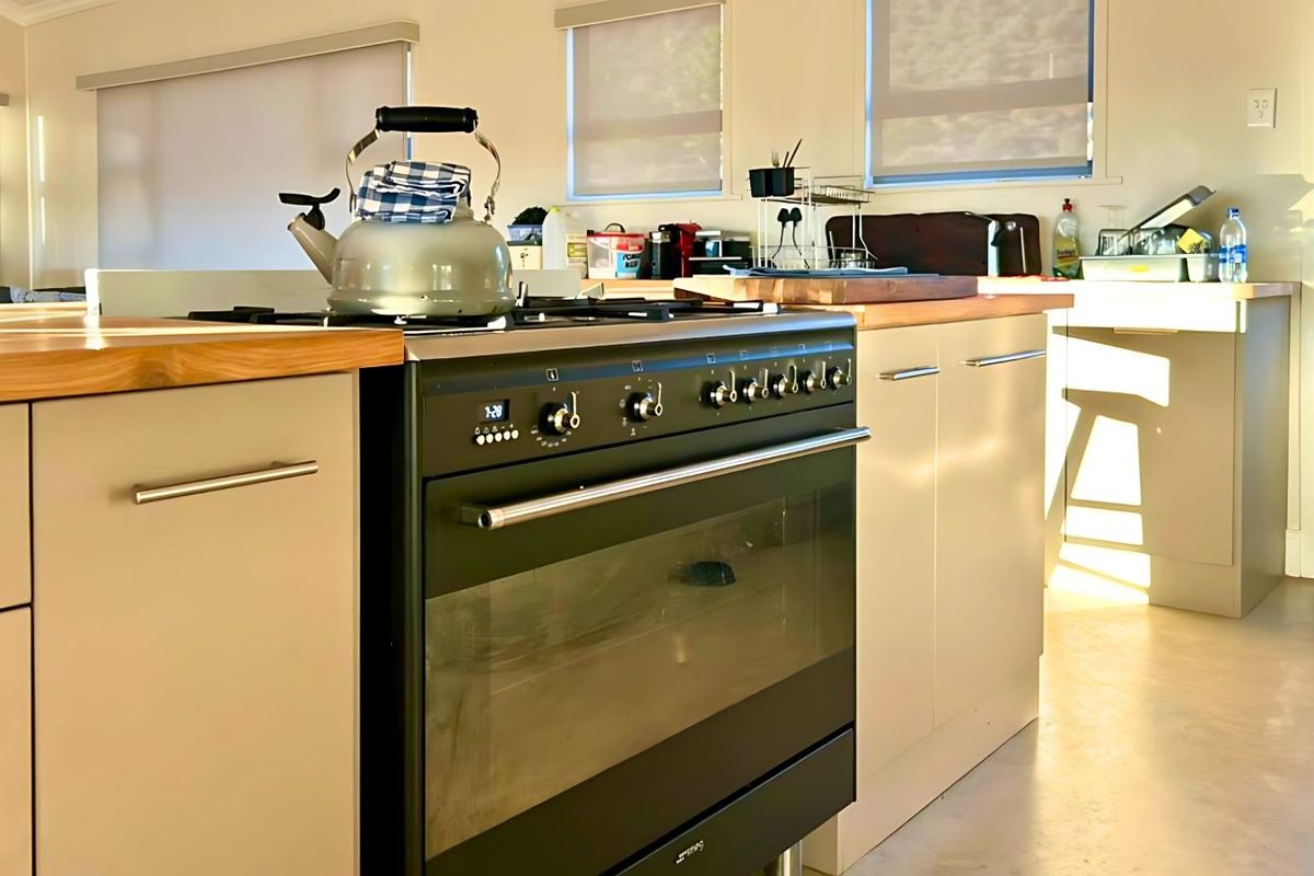 A modern kitchen featuring light-toned cabinetry, timber countertops, and a prominent black freestanding oven and gas cooktop.