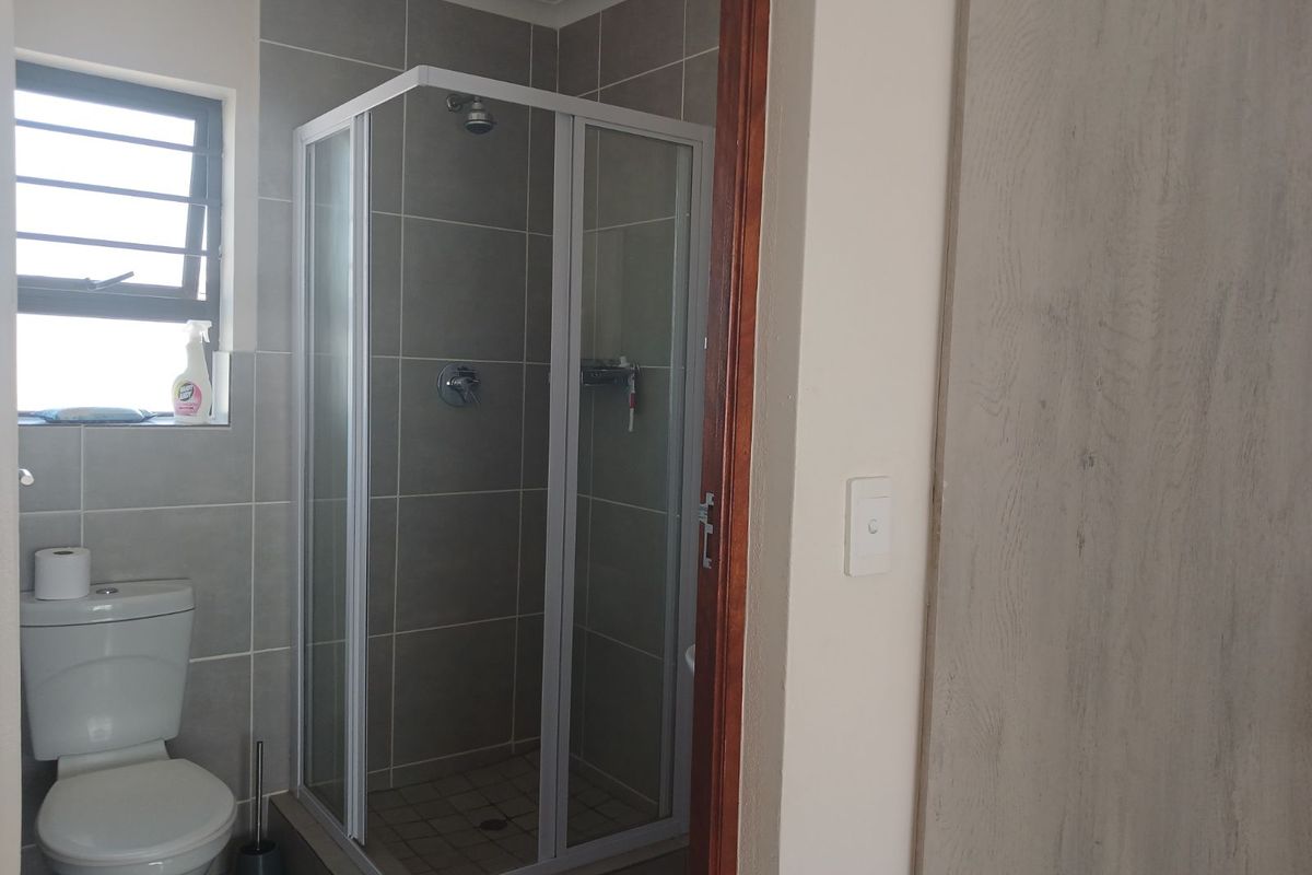A functional bathroom featuring a corner shower enclosure with tiled walls, a standard toilet, and a window for natural ventilation.