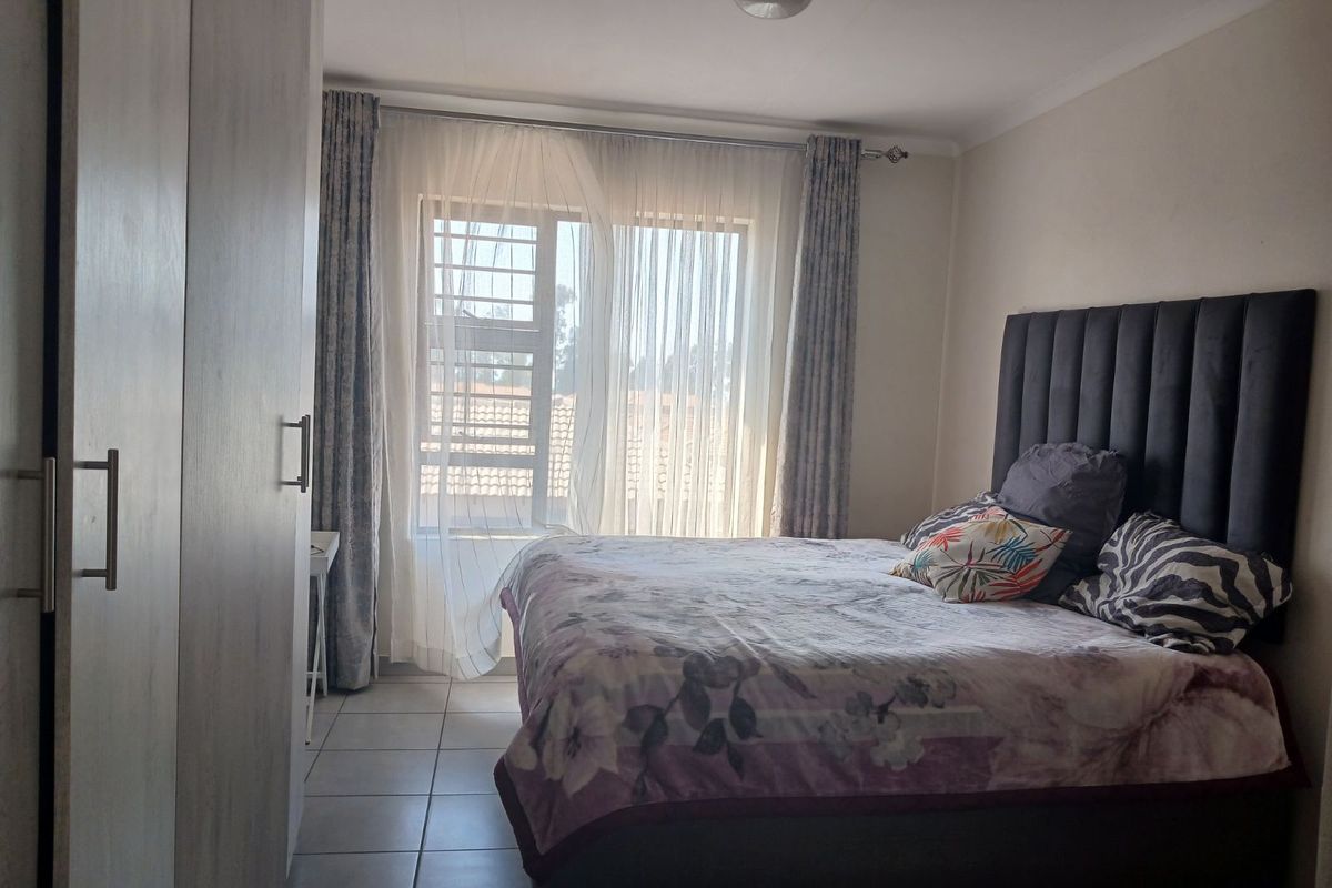 A bedroom featuring tiled flooring, built-in cupboards, and a window with security bars, providing natural light.