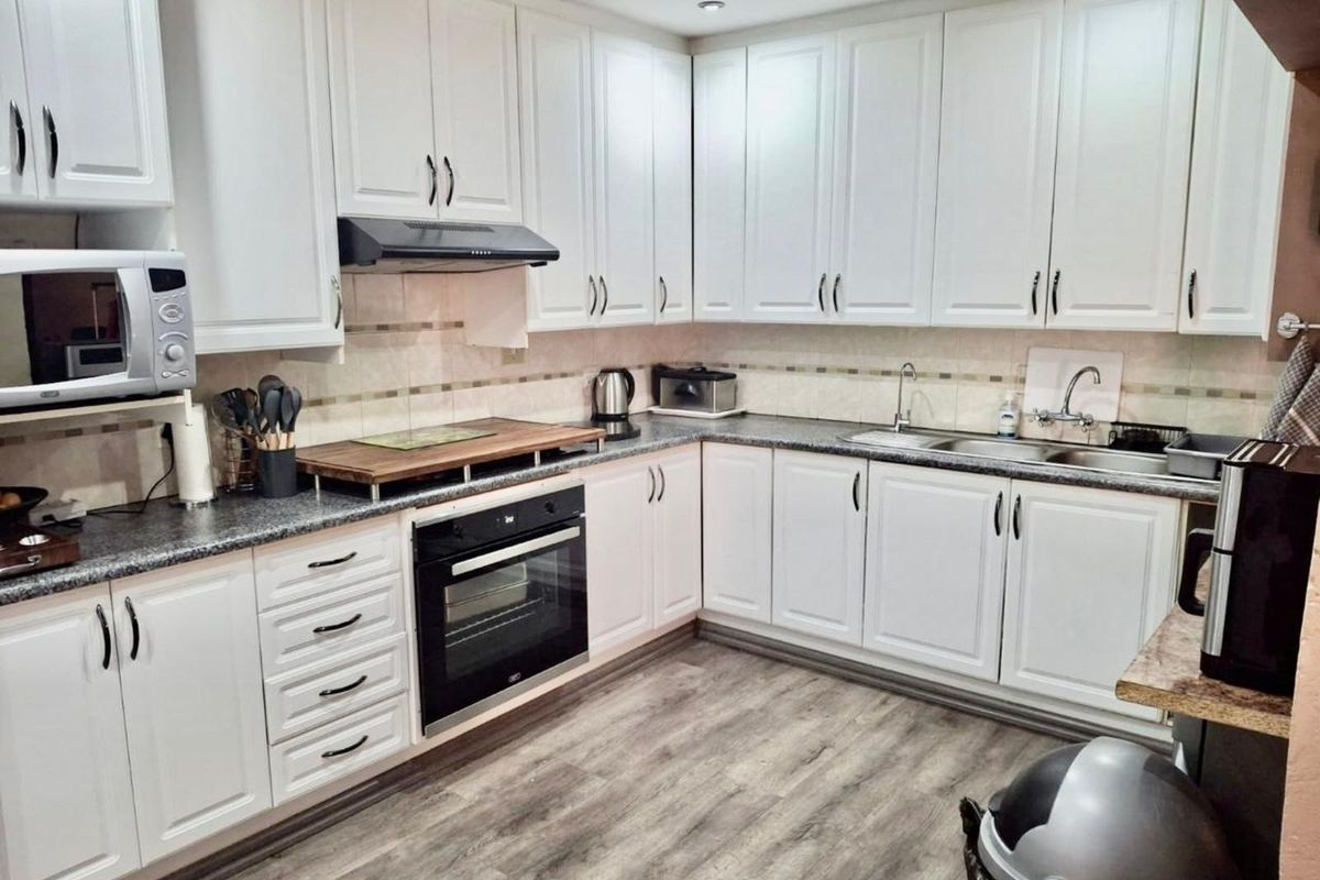 A well-maintained kitchen featuring white cabinetry, granite-look countertops, a built-in oven, extractor fan, and a double stainless steel sink.