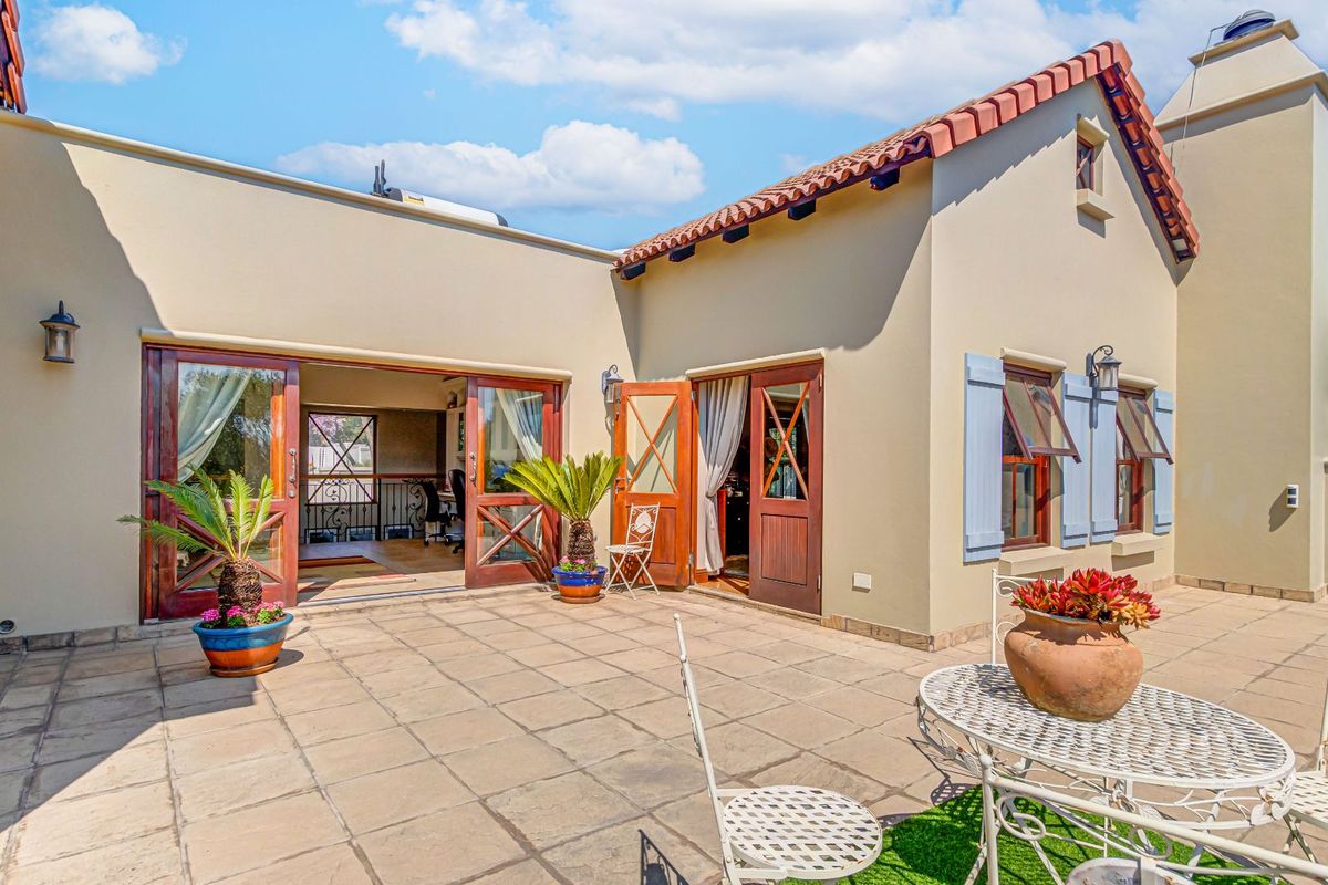 A spacious rear patio area featuring terracotta-style tiling, wooden French doors, and traditional window shutters, providing seamless indoor-outdoor flow.
