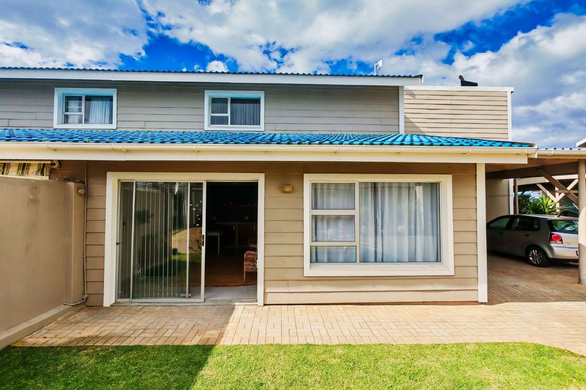 Rear view of the townhouse featuring a paved patio, sliding glass doors, and horizontal cladding with a blue tiled roof.