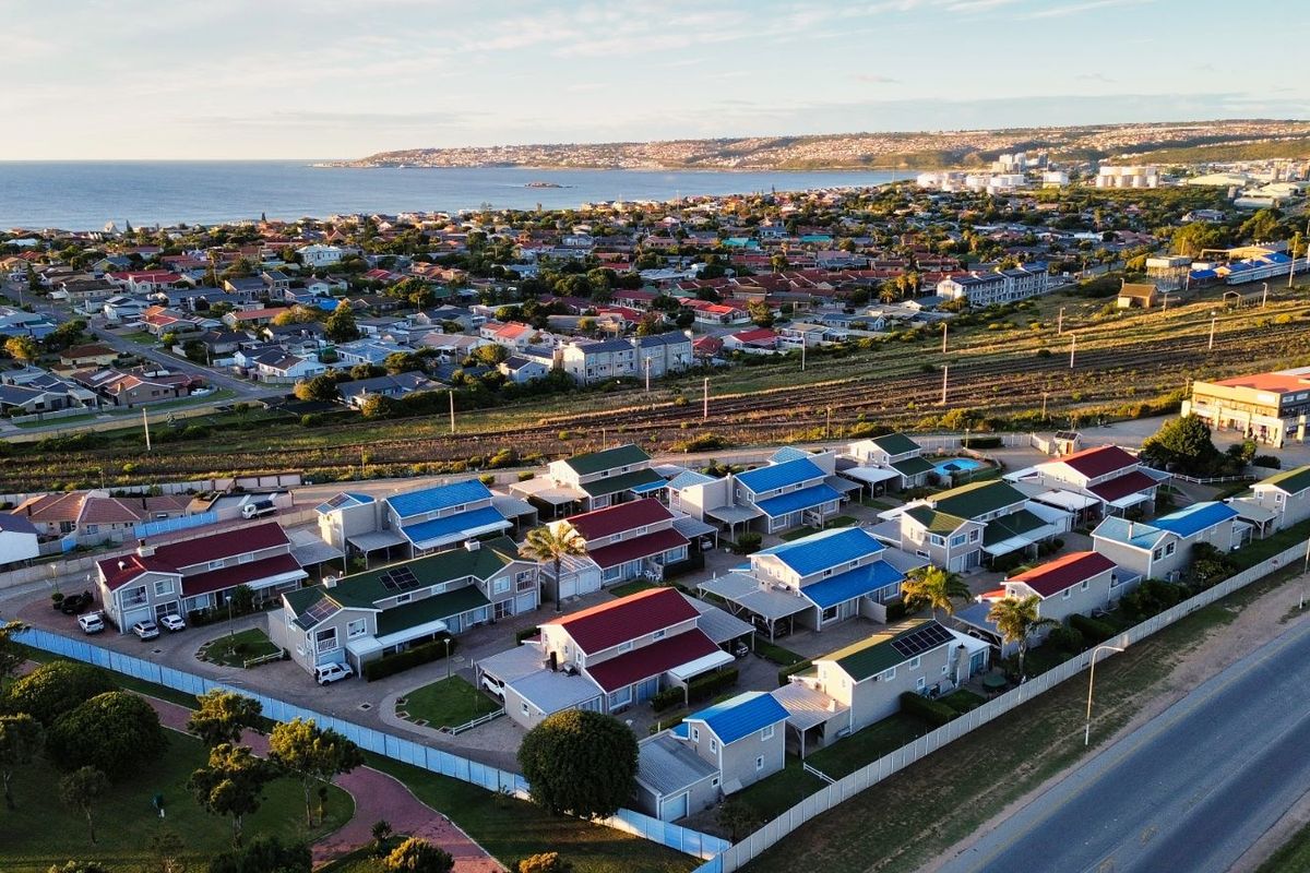 Aerial view of a residential townhouse complex featuring multiple units with pitched roofs, solar panels, and paved driveways, situated near the coastline.