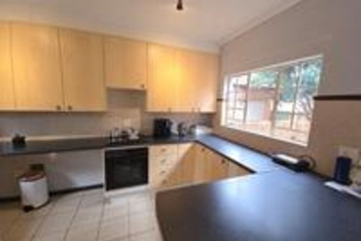 A functional kitchen featuring light wood cabinetry, dark countertops, a built-in oven, and tiled flooring with ample natural light.