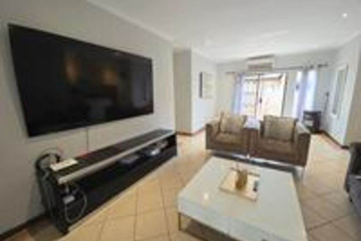 A comfortable living room featuring tiled flooring, a wall-mounted television, and sliding door access to the outdoor area.