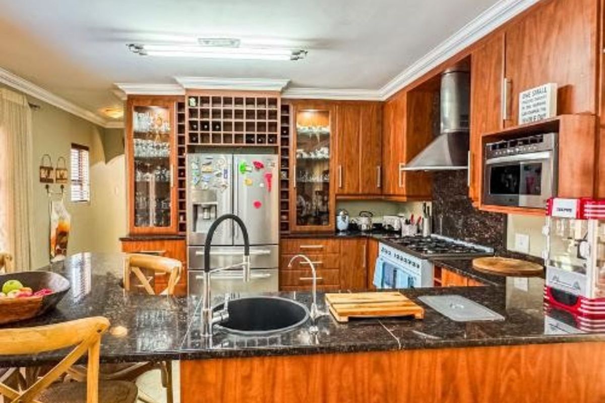 A functional kitchen featuring wood cabinetry, granite countertops, a built-in wine rack, stainless steel extractor fan, and a central island with a prep sink.