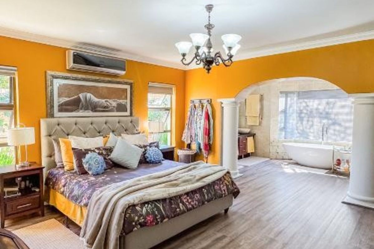 Spacious bedroom featuring an open-plan en-suite bathroom with a freestanding bathtub, separated by decorative columns and an arched entryway.