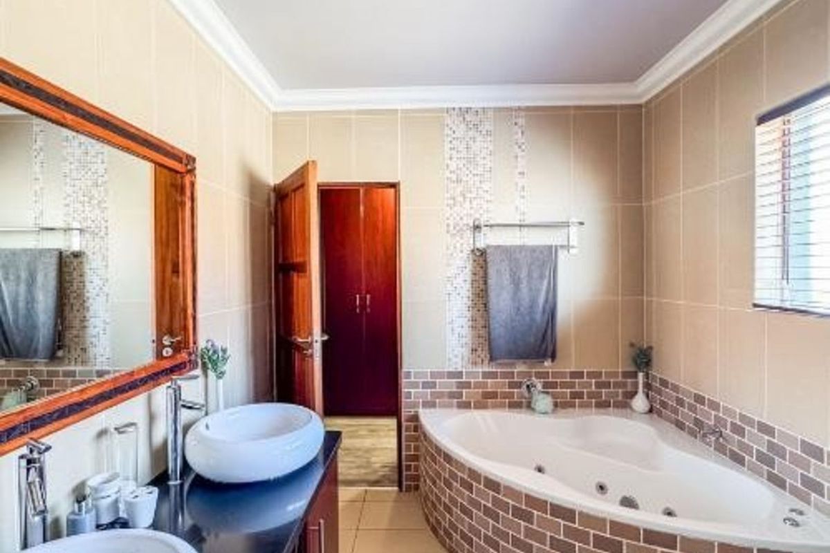 A bathroom featuring a corner jetted tub with brick-style tiling, a double vanity with vessel sinks, and neutral wall tiles.