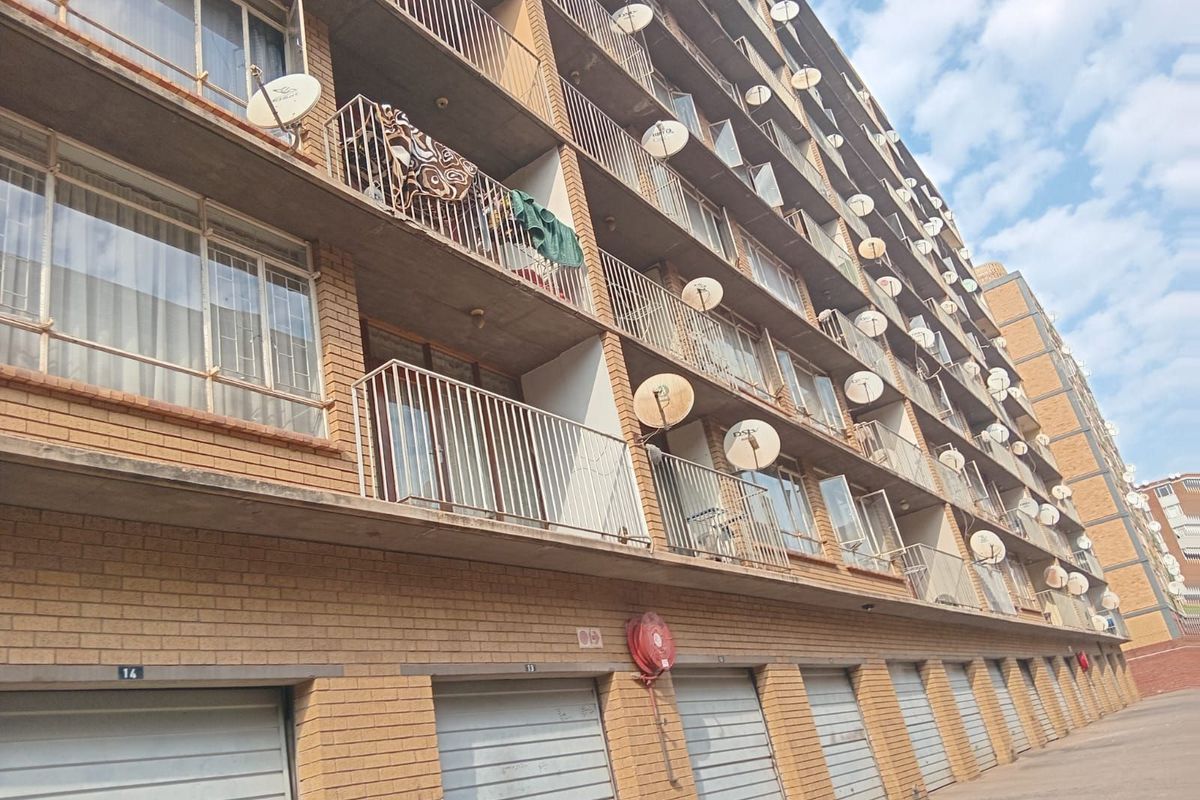 Exterior view of a multi-story apartment building featuring brick facade, private balconies with metal railings, and ground-level garage units.