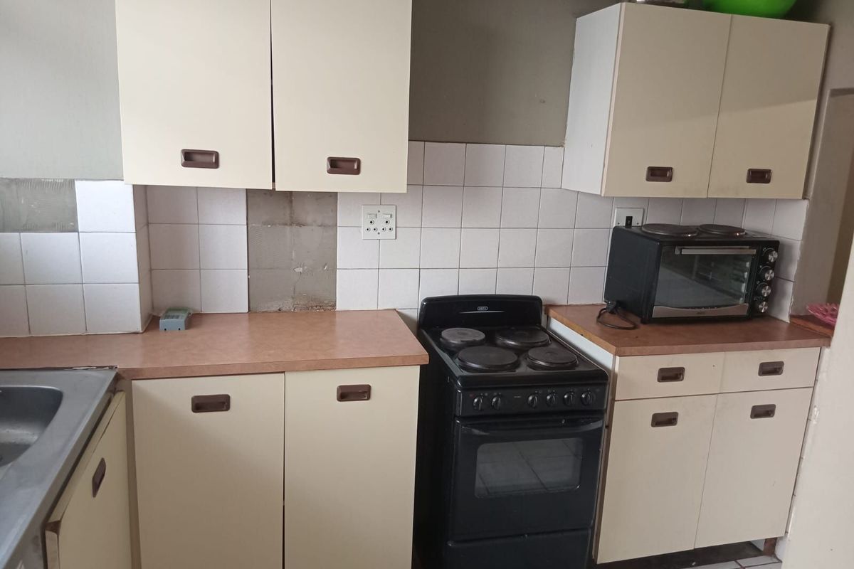 A functional kitchen featuring laminate countertops, built-in cabinetry, and a freestanding electric stove with tiled splashbacks.
