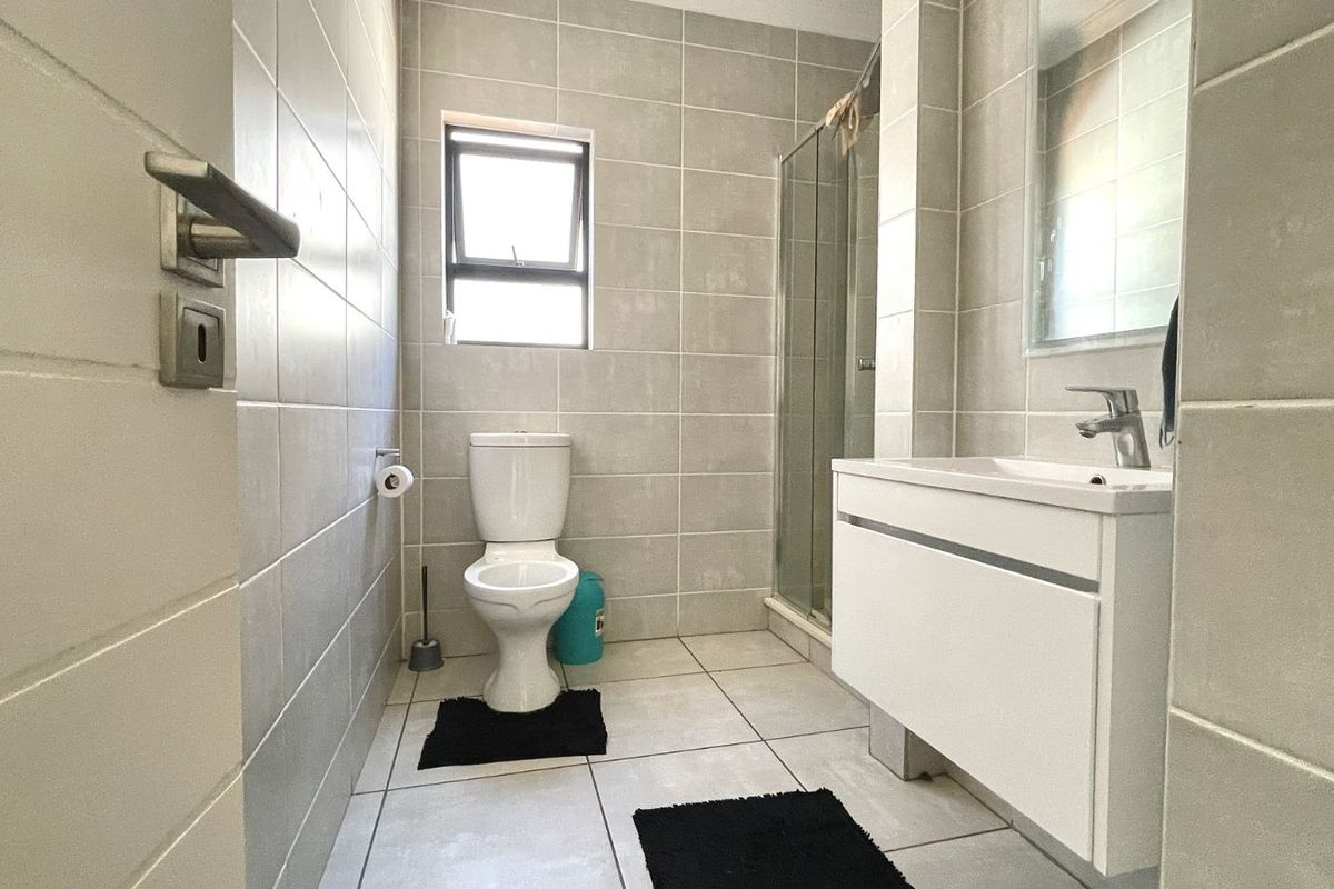 A modern bathroom featuring floor-to-ceiling grey tiling, a glass-enclosed shower, a wall-mounted vanity with basin, and a toilet.