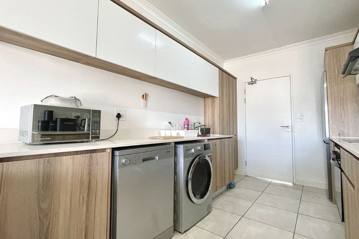 Modern kitchen featuring light wood-grain cabinetry, white countertops, tiled flooring, and integrated space for laundry appliances.