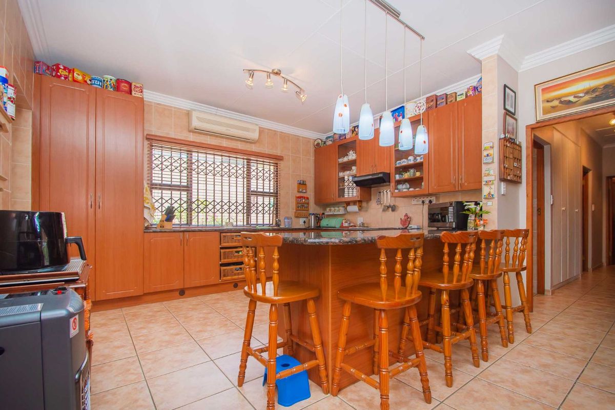A functional kitchen featuring wood-finish cabinetry, granite countertops, a central breakfast island, and tiled flooring with integrated air conditioning unit.