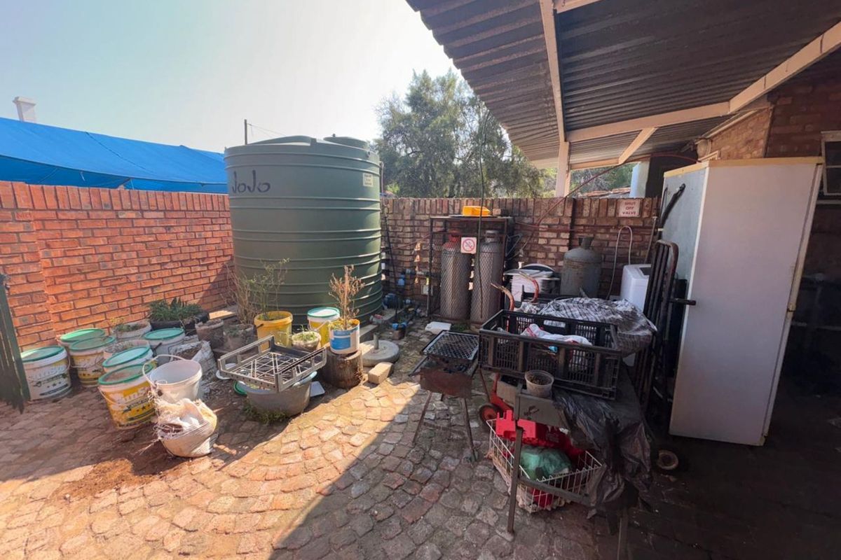 A rear utility courtyard featuring a large water storage tank, brick boundary walls, and paved flooring under a covered lean-to structure.