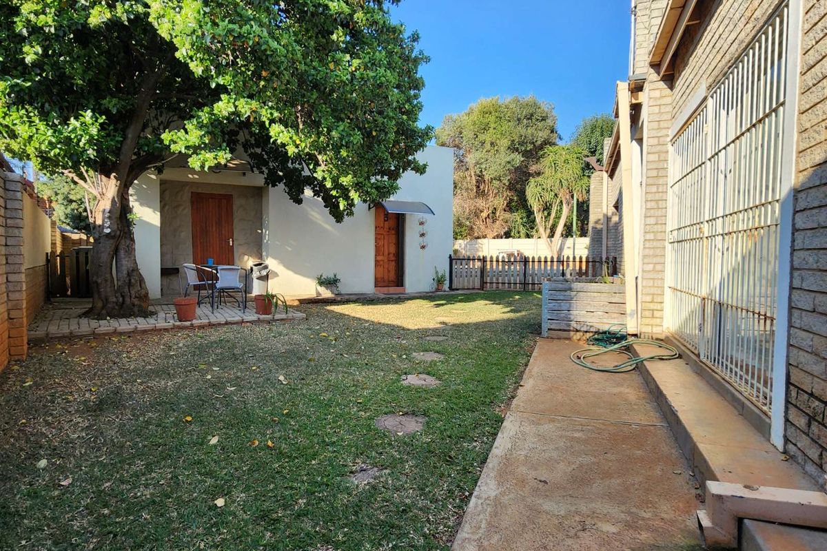 A private rear garden featuring a lawn area, mature tree, and concrete pathway adjacent to the main dwelling structure.