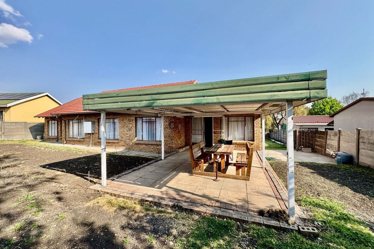 A rear view of the house featuring a covered patio area with paved flooring, overlooking a garden space.