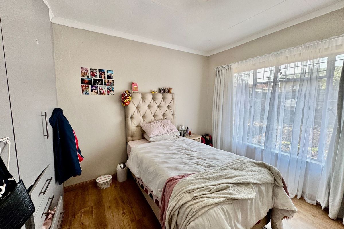A well-lit bedroom featuring wood-look flooring, built-in cabinetry, and a large window with sheer curtains, providing a comfortable and functional living space.