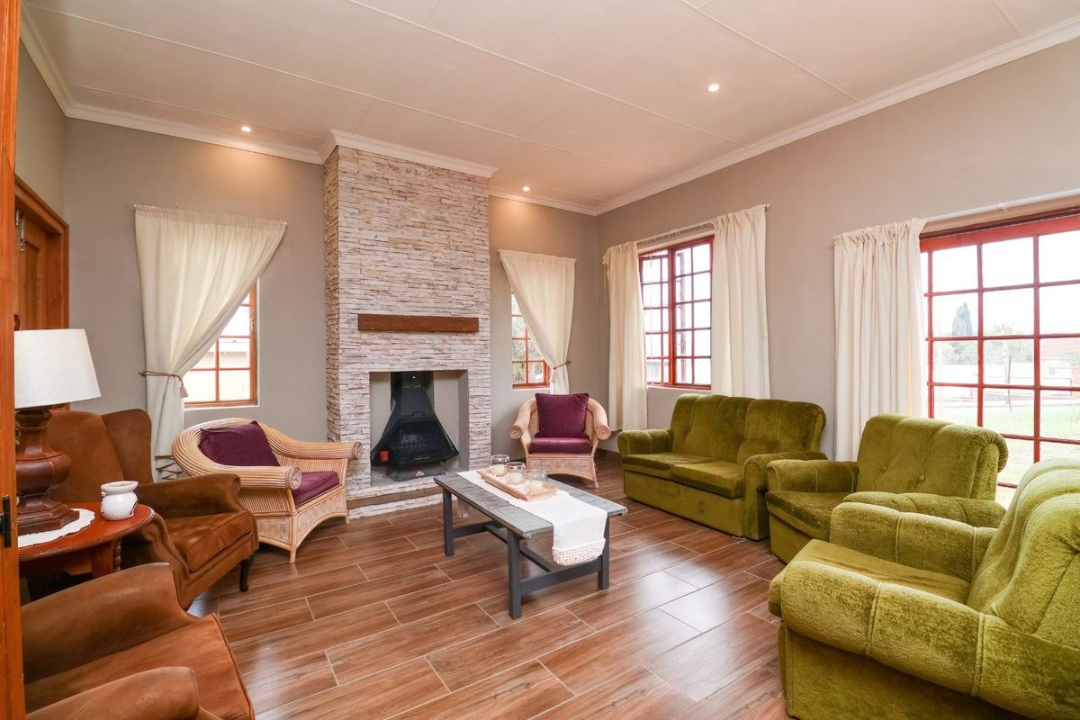 A comfortable living room featuring a prominent stone-clad fireplace, wood-look tiled flooring, and large windows that provide ample natural light.