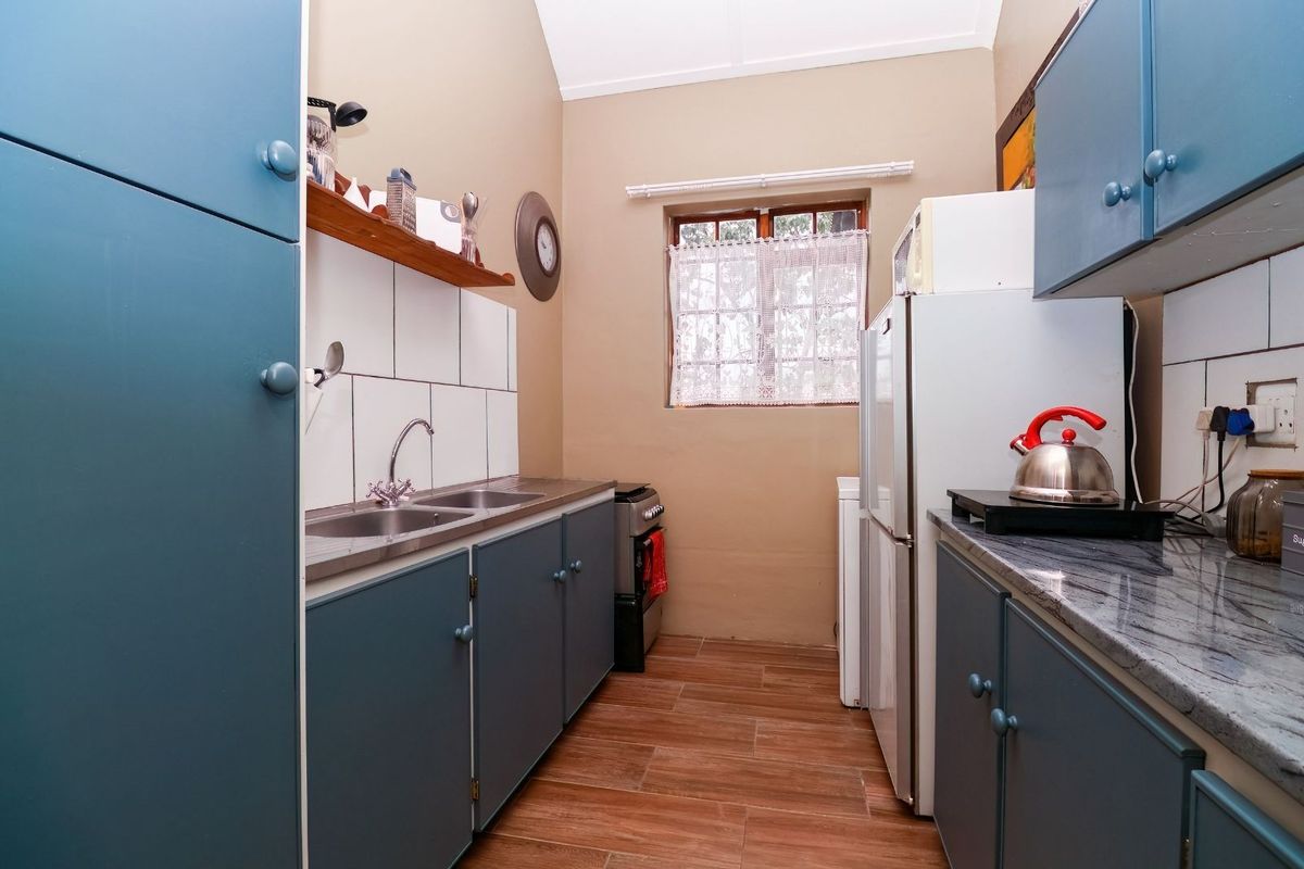 A functional galley-style kitchen featuring blue cabinetry, tiled splashbacks, a double stainless steel sink, and wood-look floor tiles.