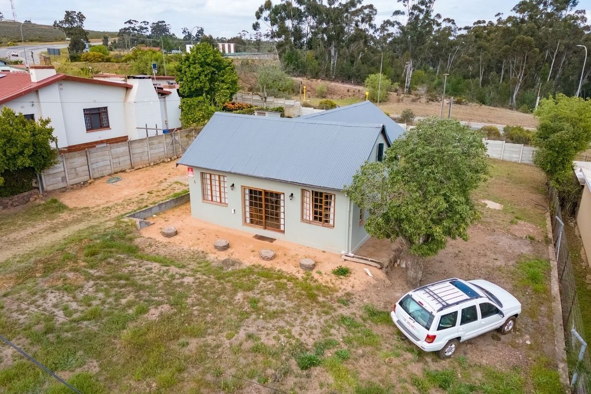 Aerial view of a detached house featuring a pitched metal roof, timber-framed windows, and sliding glass doors, set on a large, undeveloped plot.