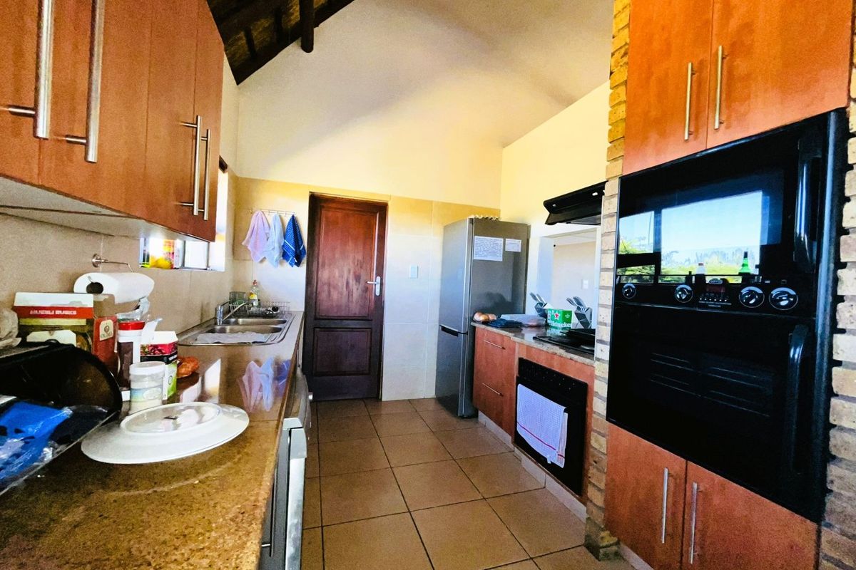 A functional kitchen featuring wooden cabinetry, granite countertops, built-in oven, and a high vaulted ceiling with exposed thatch detailing.