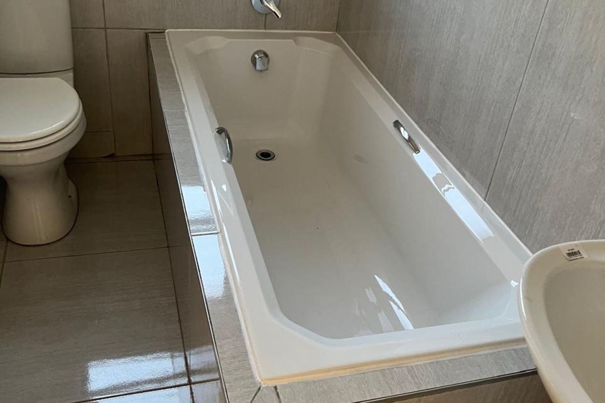 A functional bathroom featuring a built-in bathtub with tiled surround, a standard toilet, and a pedestal basin with neutral wall and floor tiling.