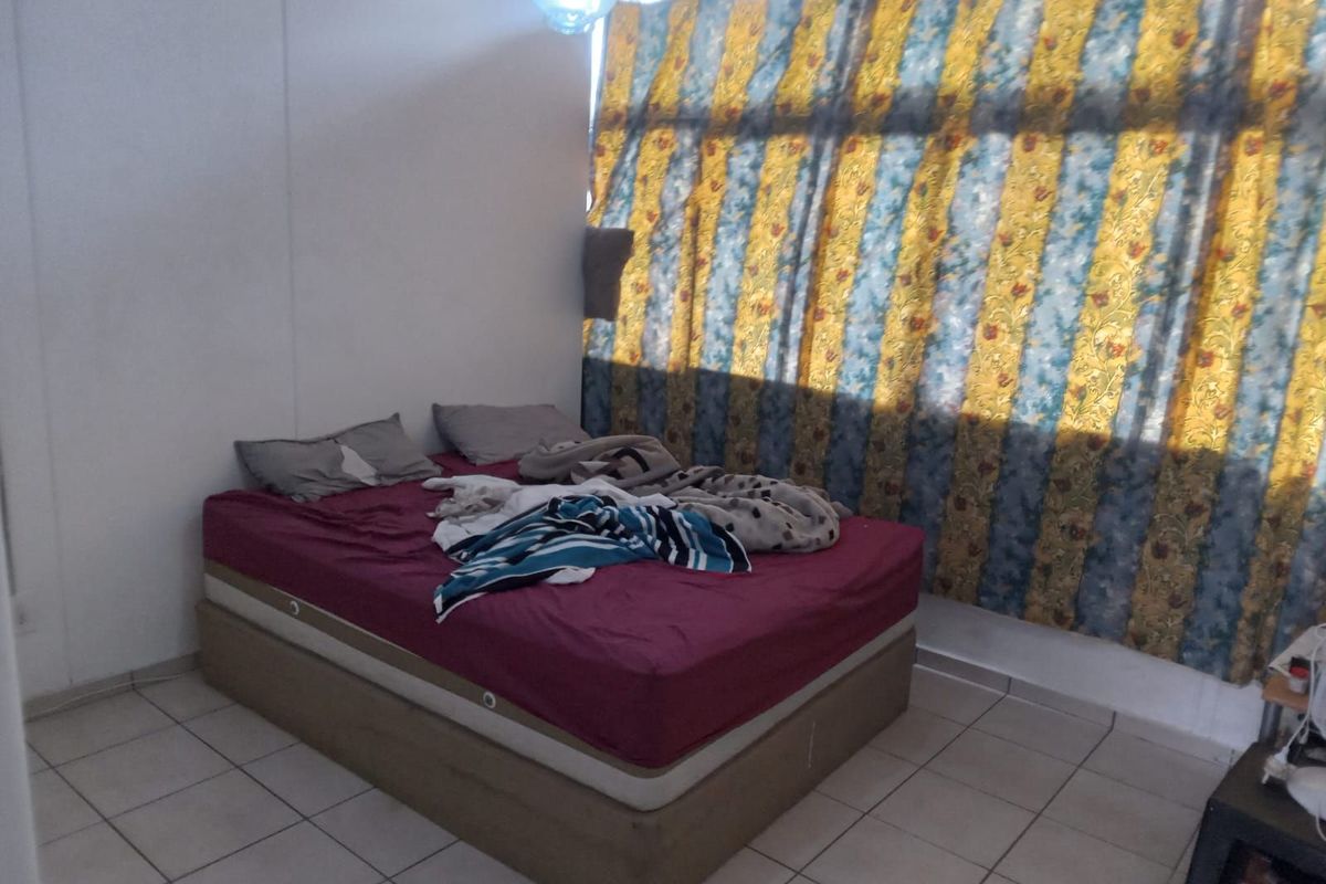 A bedroom featuring tiled flooring and large windows with patterned curtains, offering a functional space for rest.