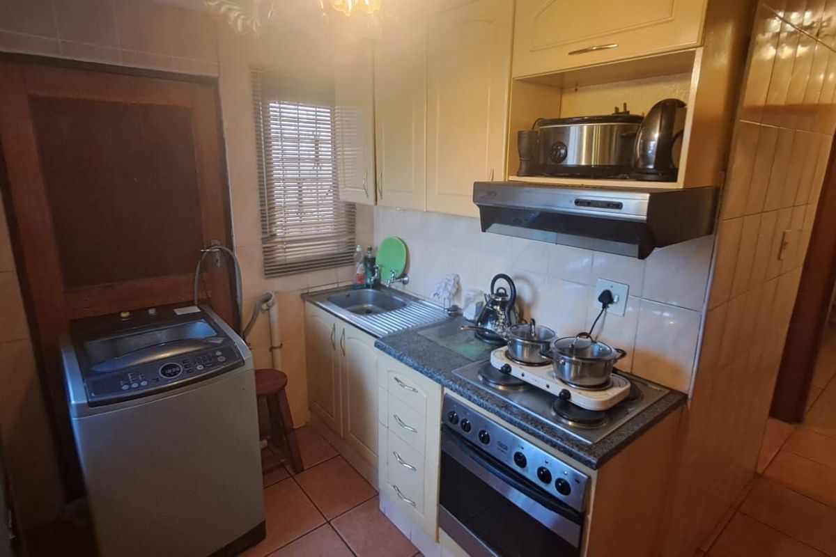 Compact kitchen featuring built-in cabinetry, a stainless steel sink, integrated stove with extractor fan, and dedicated space for a washing machine.
