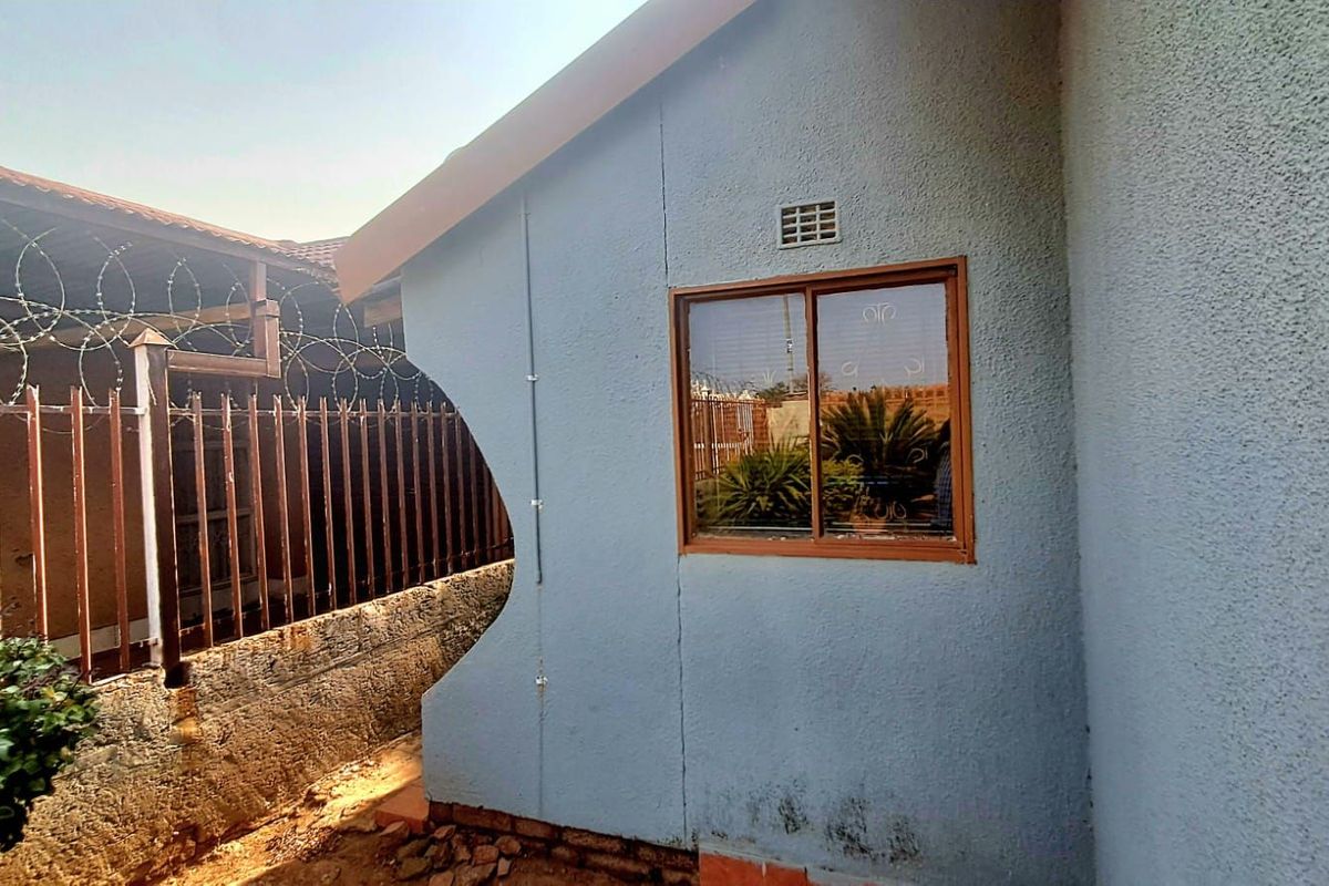 Side exterior view of the property featuring a textured blue facade, a single window, and perimeter security fencing with razor wire.