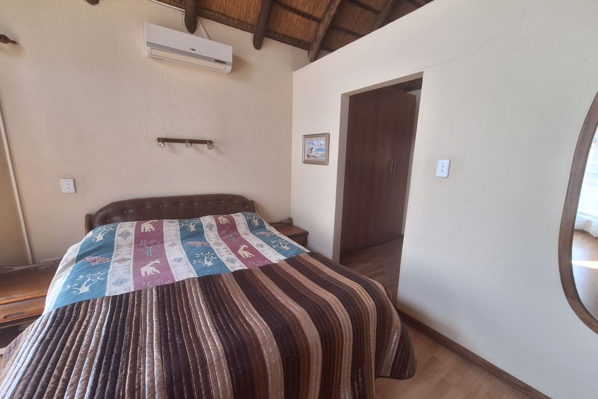 A bedroom featuring a high thatched roof with exposed timber beams, built-in wooden cupboards, and a wall-mounted air conditioning unit.