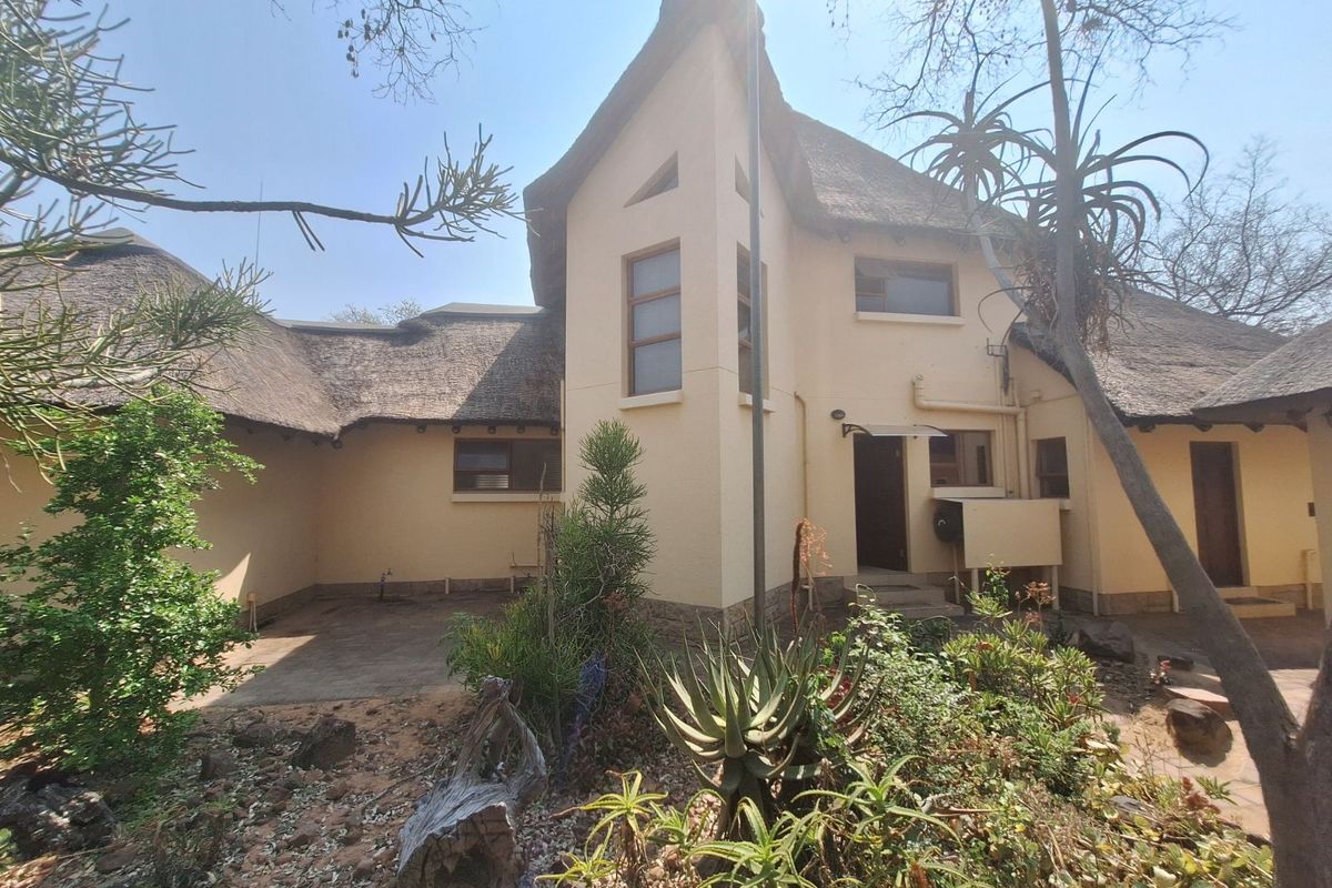 Rear view of a traditional thatched-roof house featuring a multi-level facade, paved patio area, and established garden surroundings.