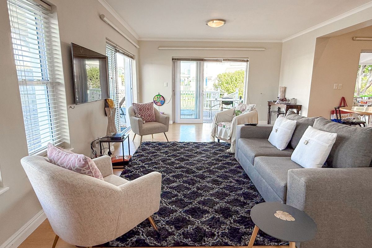Spacious living room featuring light wood-look flooring, large windows with fitted blinds, and sliding glass doors providing direct access to the outdoor patio area.