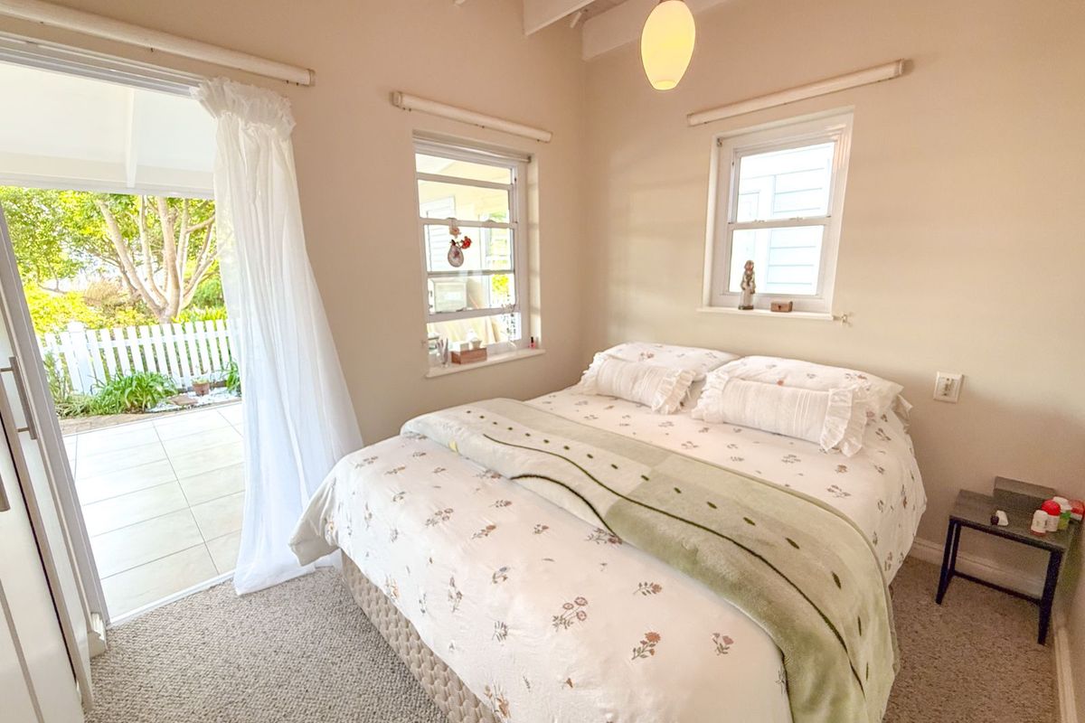 A cozy bedroom featuring exposed ceiling beams, carpeted flooring, and direct access to an outdoor patio area through a glass door.