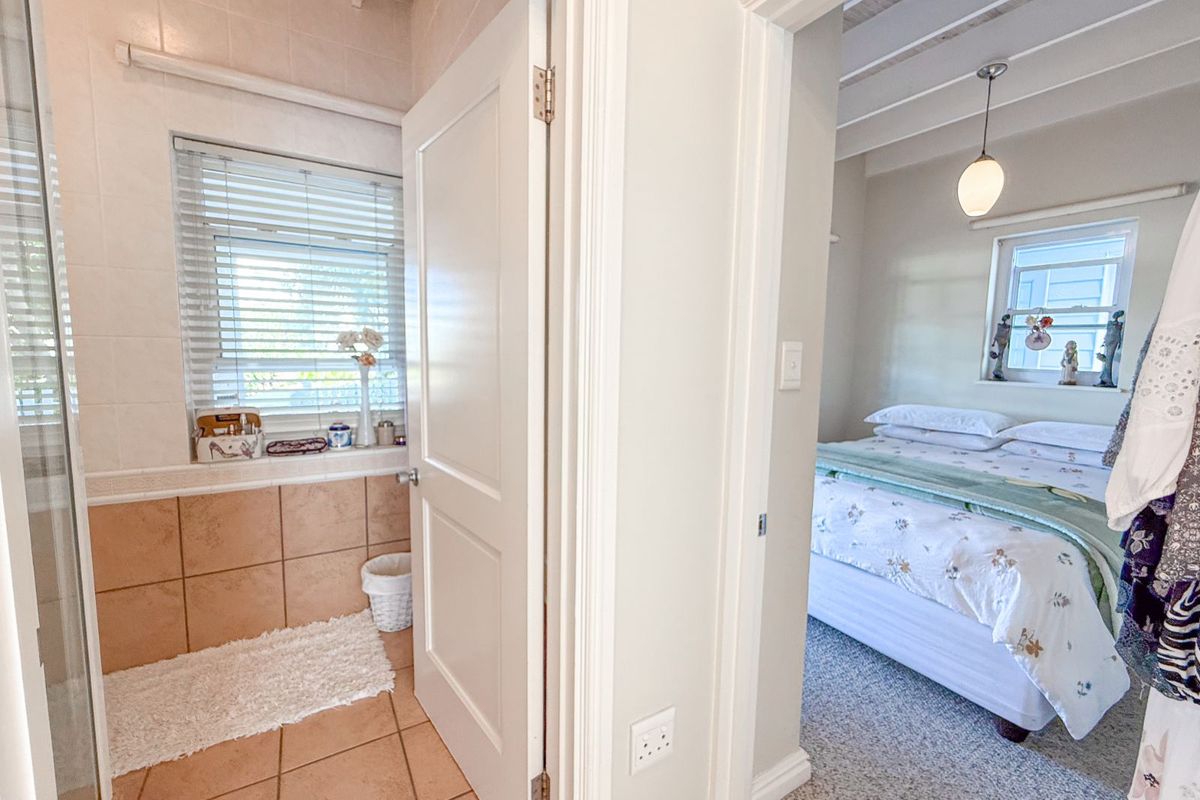 A view from a tiled bathroom looking into an adjacent bedroom with exposed ceiling beams and carpeted flooring.
