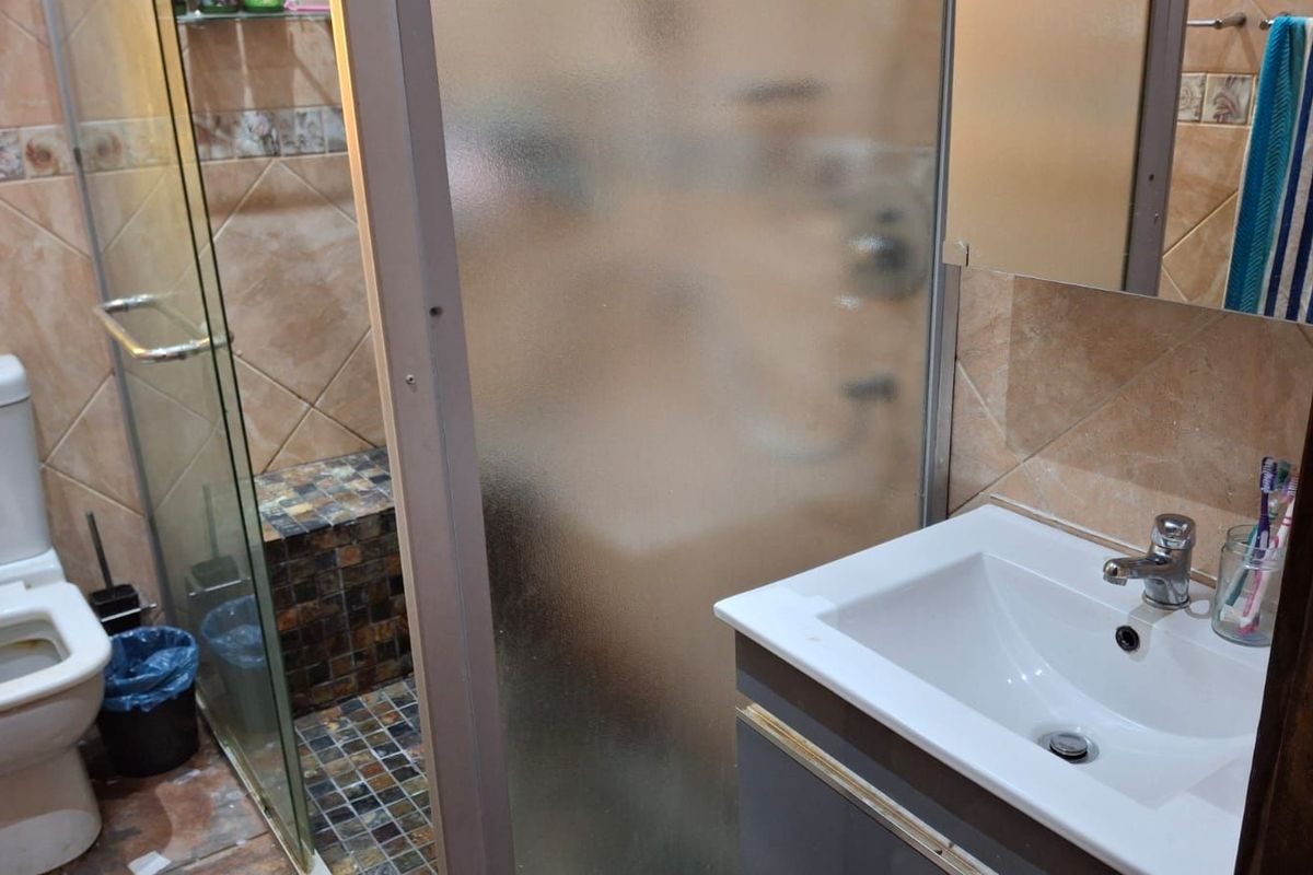 A functional bathroom featuring a glass-enclosed shower with mosaic tiling, a modern vanity basin, and a standard toilet.